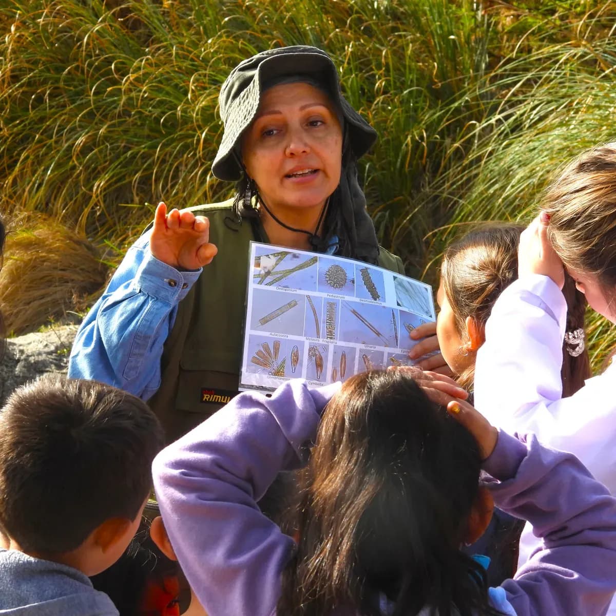Una educadora muestra una lámina a un grupo de chicos en el campo.