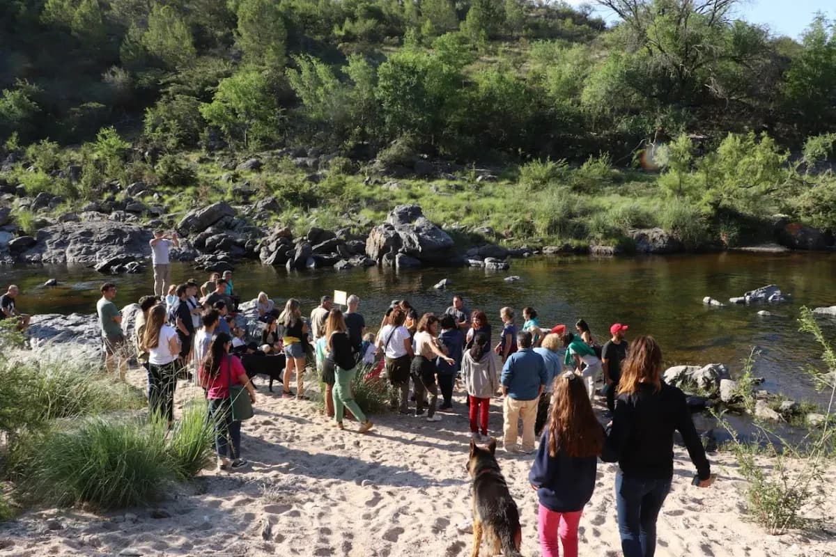 Un grupo numeroso de personas reunido en la orilla arenosa del río.